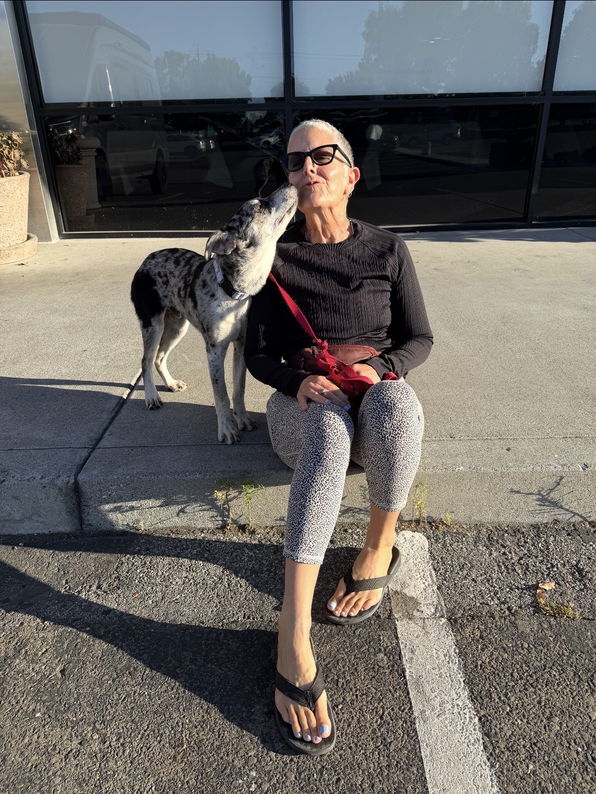 Virginia seated outdoors as a spotted dog affectionately licks her face